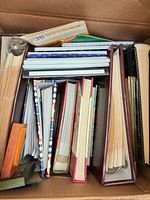 Box filled with assorted empty photo albums, showing variety of sizes, colors and bindings