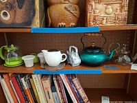 Shelf showing various teapots, kettle, drippers and books