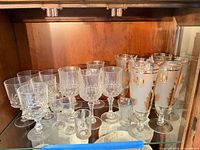Group of cut crystal goblets, cordials, and frosted gold leaf stemware on shelf