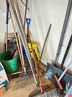 Group of rakes, shovels, bucket and other tools leaned against wall