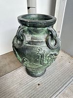 Full view of cast metal pot showing verdigris finish, ring handles, relief decoration