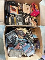 Overview of two boxes filled with assorted DVDs showing variety of titles and cases