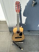 Front view of Nova acoustic guitar standing upright with recorder at base