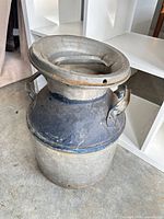 Full view of vintage metal milk can showing lid, handles, body, and patina