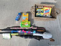 All items grouped on pavement showing basket with contents, cleaning supplies, umbrellas, cane and duster