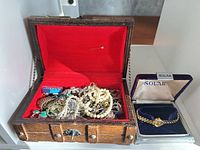 Open wooden chest with assorted jewelry and Solar watch box beside it