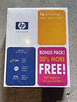 Front view of sealed HP printing paper ream showing size, weight, brightness, and 600-sheet bonus details