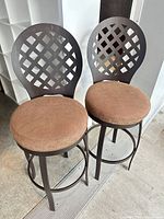 Two metal swivel bar stools with lattice backs and brown upholstered seats