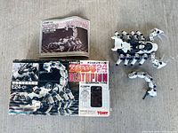 Box, instruction manual and assembled Zoids Deathpion figure with detached tail segment displayed on surface