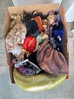 Box containing five porcelain dolls with assorted outfits, pillow, stand