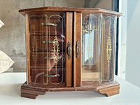 Front view of wooden jewelry box with glass doors and gold scrollwork