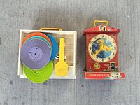 Record player with stacked colored discs and yellow tone arm next to red Fisher-Price teaching clock