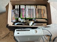 Box containing Xbox 360 console, controllers and rows of game cases