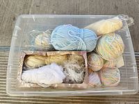 Overview of clear bin containing assorted yarn skeins and wool roving
