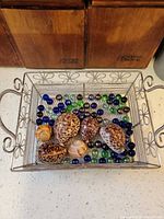 Top view of metal tray holding glass marbles and seashells