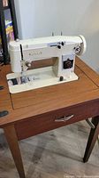 Domestic sewing machine installed in open fold-out cabinet