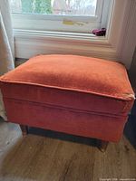 Full view of burnt orange velvet ottoman beside window