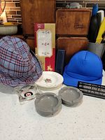 Lot overview showing two caps, concrete ashtrays, glass ashtray, porcelain dish and boxed handkerchiefs