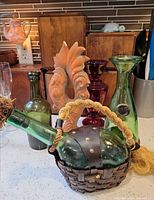 Overall lot showing green demijohn in wicker, slim green bottle, green bud vase, ruby vase and terra-cotta rooster