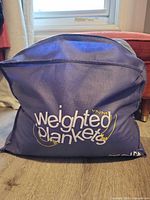 Navy zippered storage bag labeled “weighted blanket” sitting upright on floor
