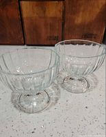 Front angled view of both clear glass dessert dishes showing shape and footed bases