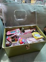 Closed green metal sewing box with clear plastic lid showing contents