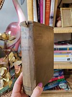 Front and spine view of cloth-bound book showing title, author and publisher with spine fraying