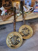 Two brass fruit-motif plaques with wood handles on shelf
