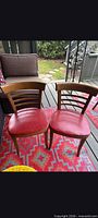 Front view of both wooden chairs showing red vinyl seats and slatted backs