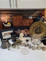 Overview of brass charger, silver bowl, wooden canisters, figurine, goblet, scoops, framed needlepoint