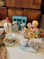 Overall lot view showing figurines, teacup, saucer, baby bottle bank, decor panel, scarf