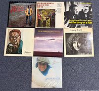 Group shot of seven album covers displayed on floor