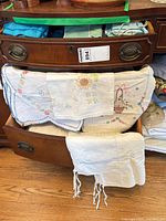 Linens displayed on and in dresser showing embroidered tablecloths, dresser scarves and fringed piece