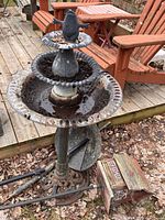 Full view of three-tier bird bath fountain with pump cord, rust and dirt visible; wood birdhouse on post lying nearby