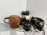 Grouped shot of all items on shelf: Canon camera, Minolta lens, flash with box, leather lens case, soft pouch, accessories