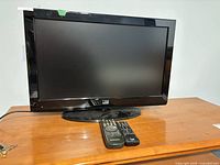 Front view of Fluid 26" LCD TV on stand with two remotes