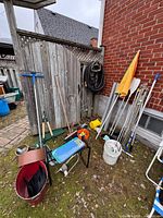 Overall lot showing garden tools, hose, kneeler, red trug, watering can and fence backdrop