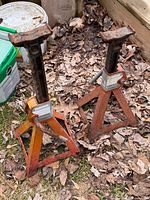 Two adjustable metal Canadian Tire jack stands on ground among leaves