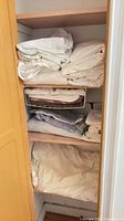 linen closet shelves with folded white and cream sheets, pillowcases, beige and grey towels