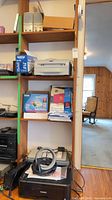 Shelving with printers, toner, scanner, router box, paper, APC UPS, Canon printer with headphones