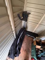 Folded camping table inside black carry bag beside load assist arms leaning in shed corner