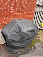 Grill with black cover in place against brick wall