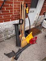 All items leaning against wall including leaf blower, shovels, brooms