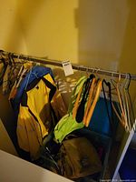 Closet rod with yellow rain coat, blue jacket, green vest, multiple hangers and tote containing bag