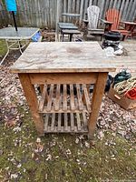 Front view wood kitchen cart, butcher-block top, two slatted shelves, casters visible
