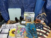 Lot overview showing boxed feeder, PartyLite box, metal wall art, garden flag