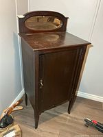 Front view of dark wooden music cabinet showing single door and oval mirror backsplash