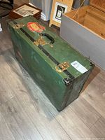 Full view of green metal trunk closed, showing handle, latches and edge bands
