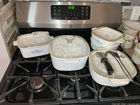 Group view of all five casseroles, four lids and two lifters on stove