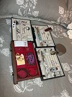 Overview showing four trays with assorted jewelry pieces on bed
